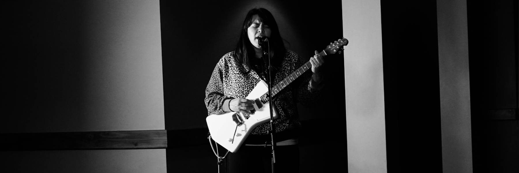 Black and white photo of a female singer with a white, electric guitar